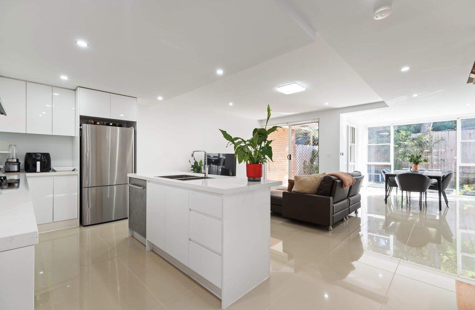 Kitchen with white cabinetry and beige floor tiling opening to lounge and dining with brown leather sofas. This was the top apartment sale in Gordon in May 2026